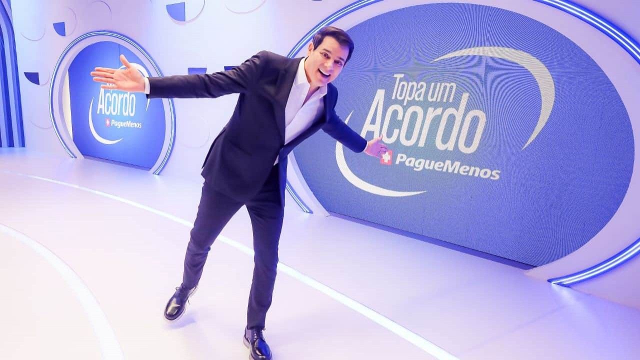 Celso Portiolli no cenário de seu novo game-show, sorrindo, com os braços abertos