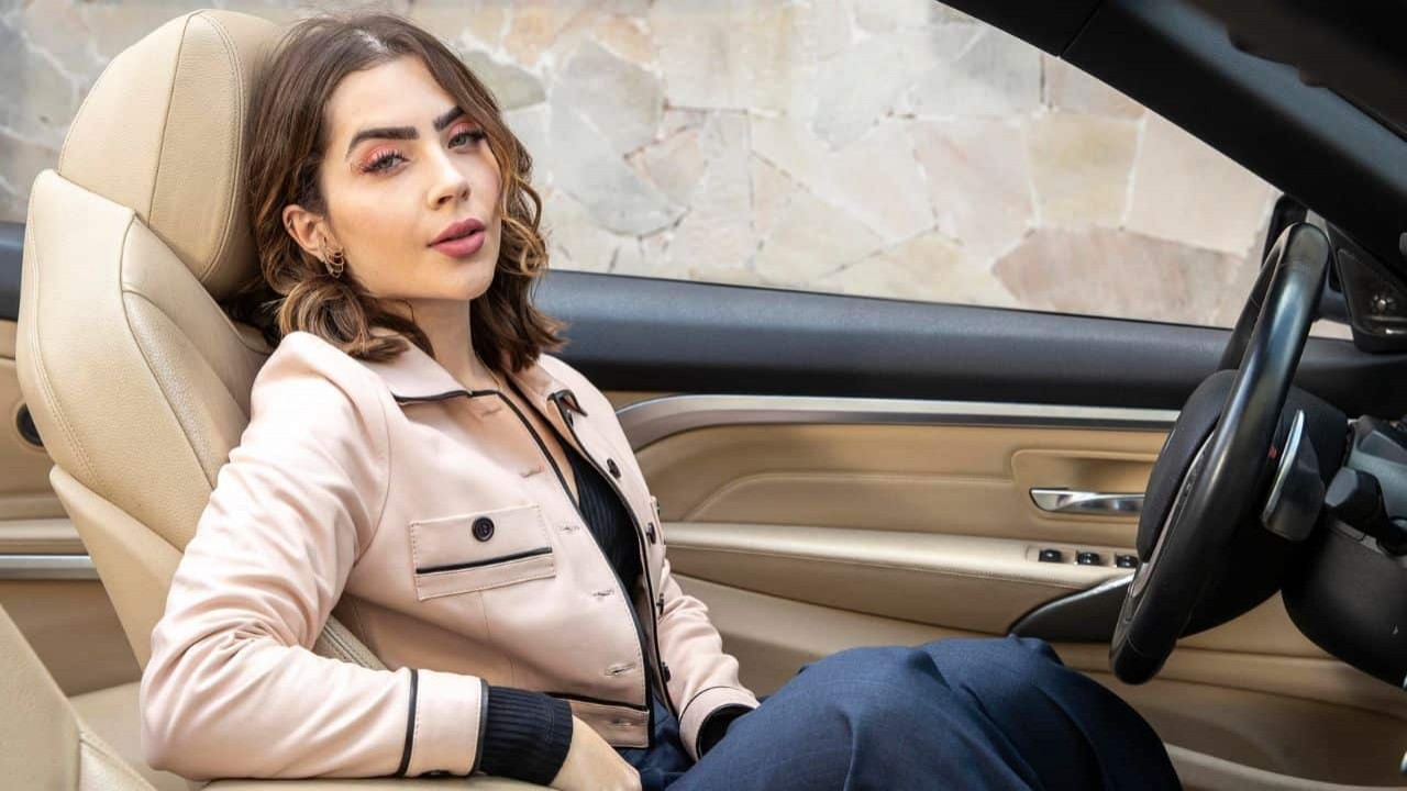 Jade Picon de blazer rosa sentada dentro de carro e posando para foto sem sorrir