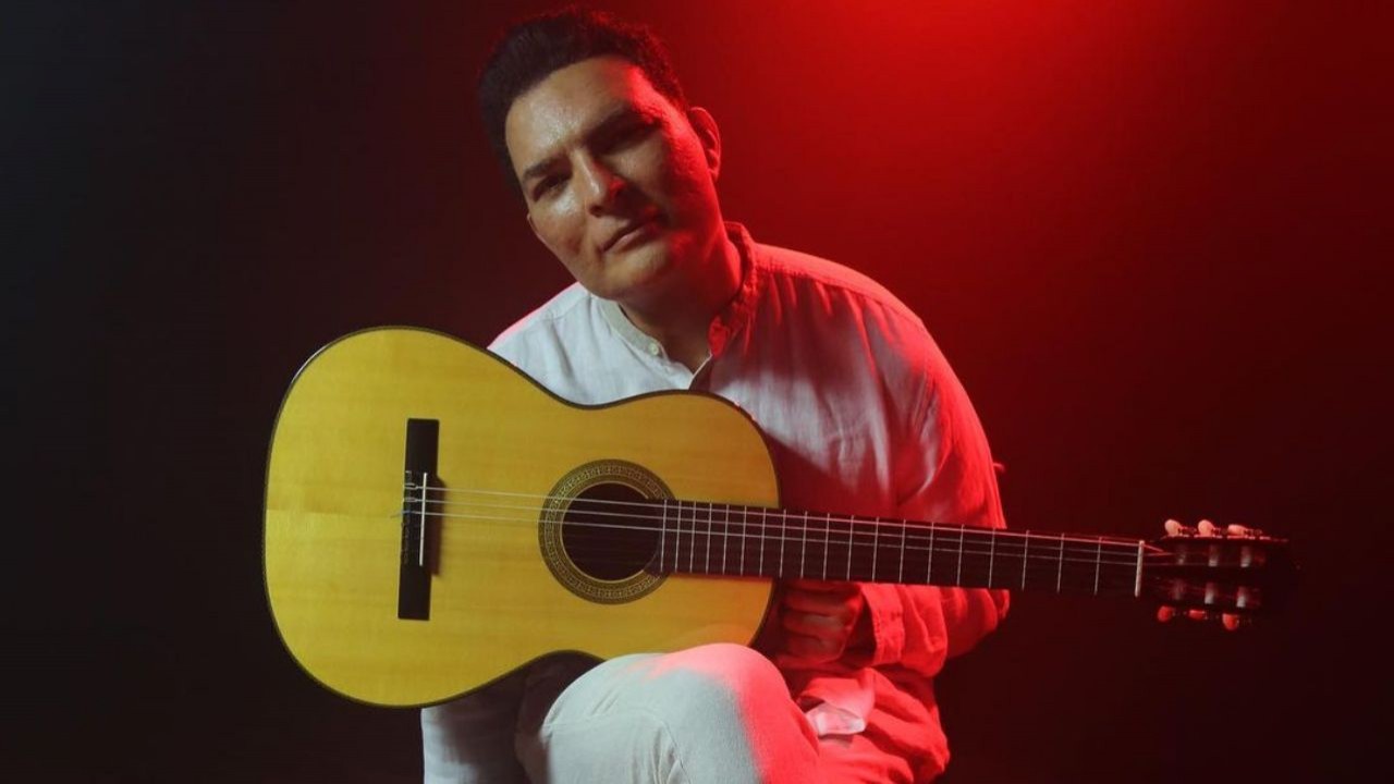 Leandro Lehart posando para foto sentado, vestindo roupa branca e com violão