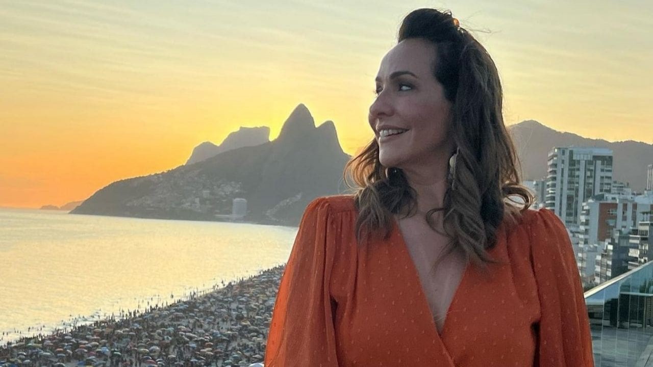 Maria Beltrão de blusa coral e cabelos soltos, posando para foto de perfil com paisagem ao fundo