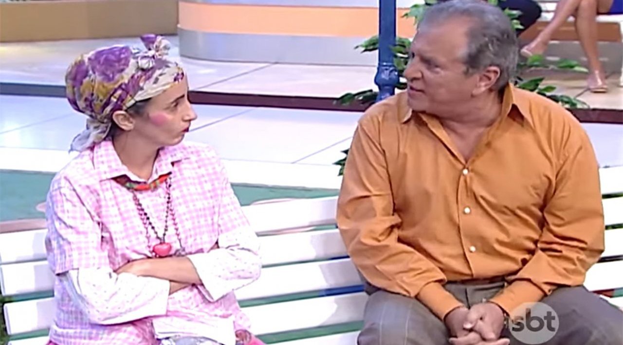 Filó (Gorete Milagres) e Carlos Alberto de Nóbrega sentados no banco da Praça É Nossa olhando um para o outro