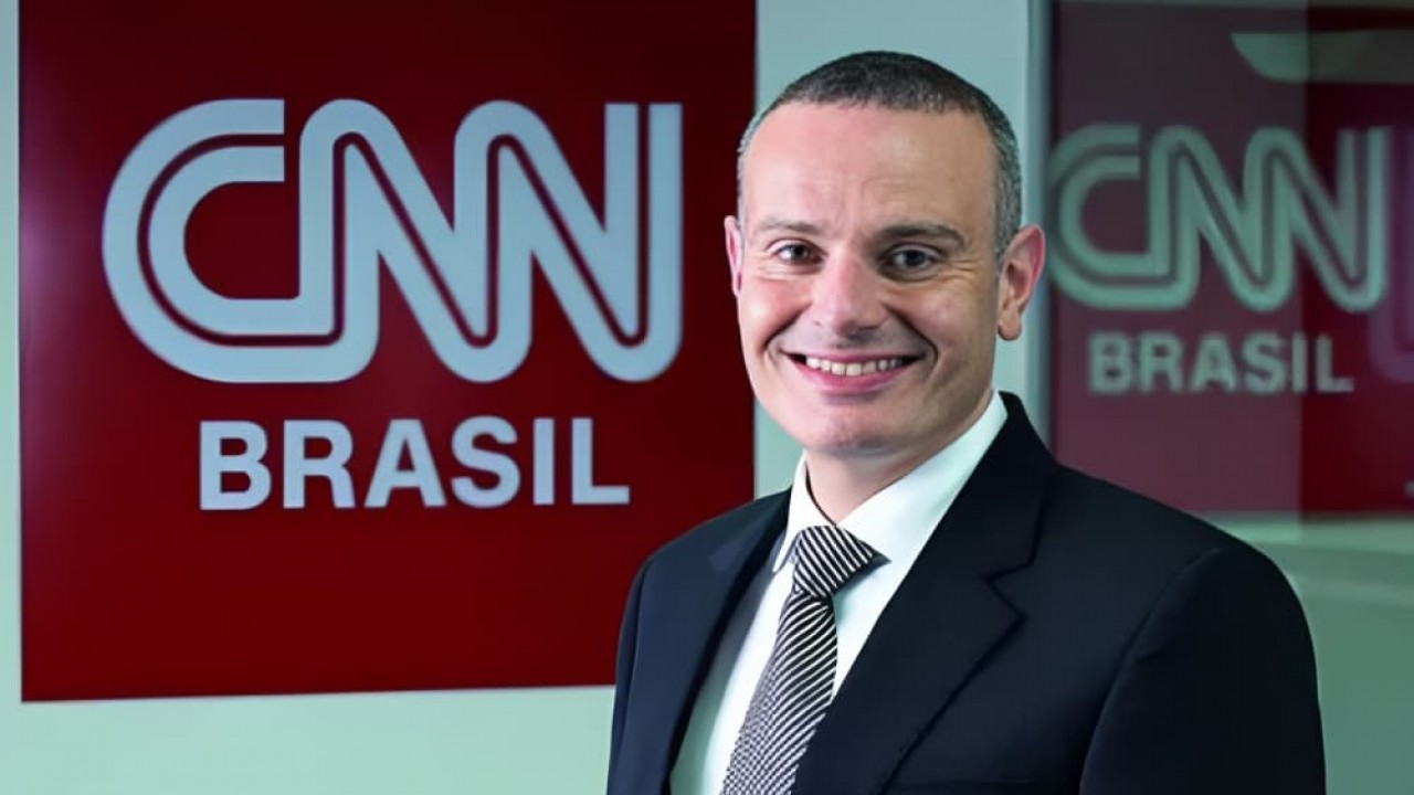 Leandro Cipoloni sorrindo perto de placa da CNN Brasil