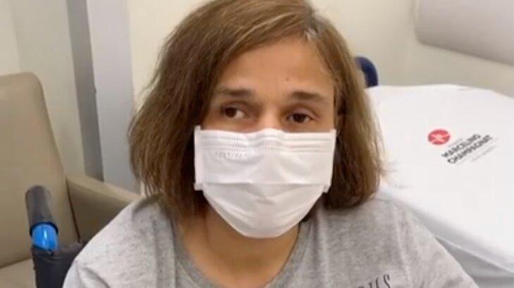 Claudia Rodrigues aparece de máscara, sentada em cadeira de rodas, em quarto de hospital