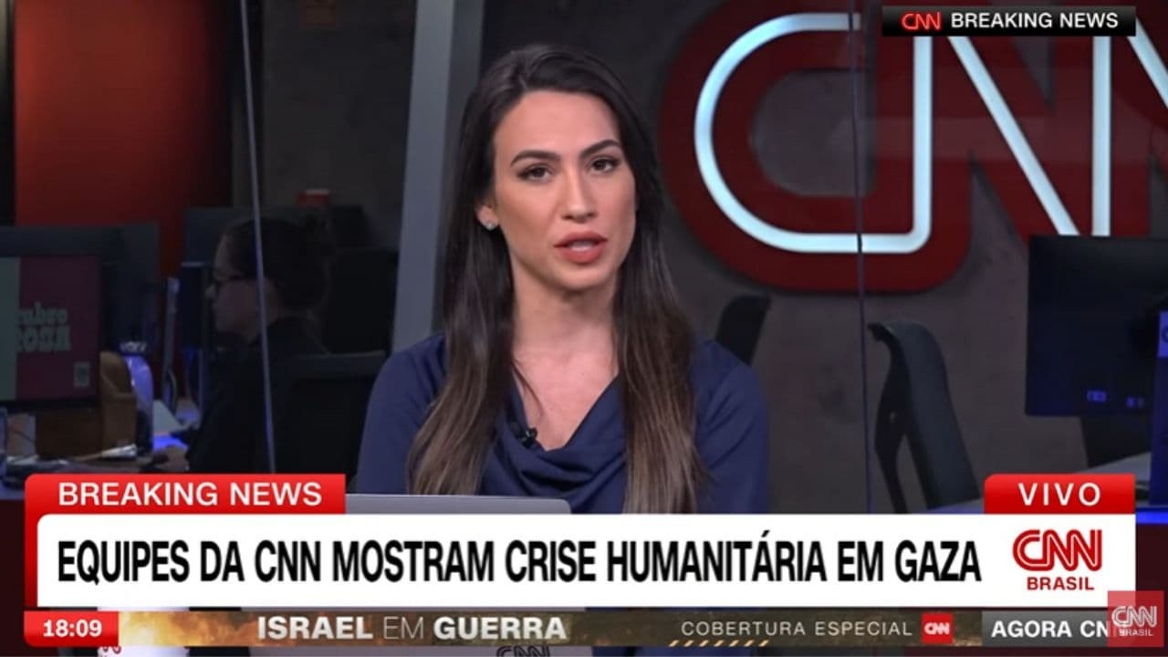 Tainá Falcão ao vivo pela CNN Brasil com cabelo solto e blusa azul, tela com GCs