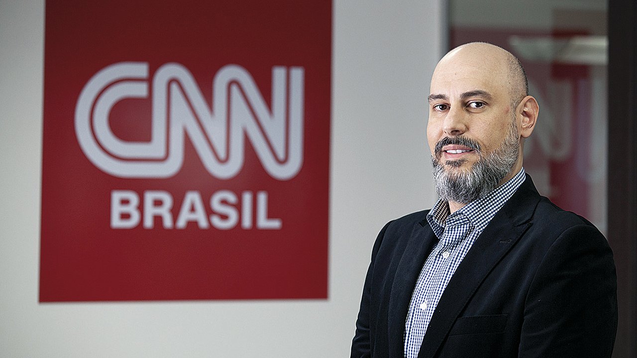 Douglas Tavolaro posando para fotos tendo ao fundo a logo da CNN Brasil