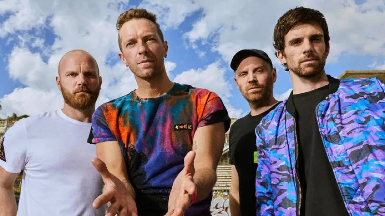 Banda Coldplay em foto de divulgação com o céu com nuvens ao fundo