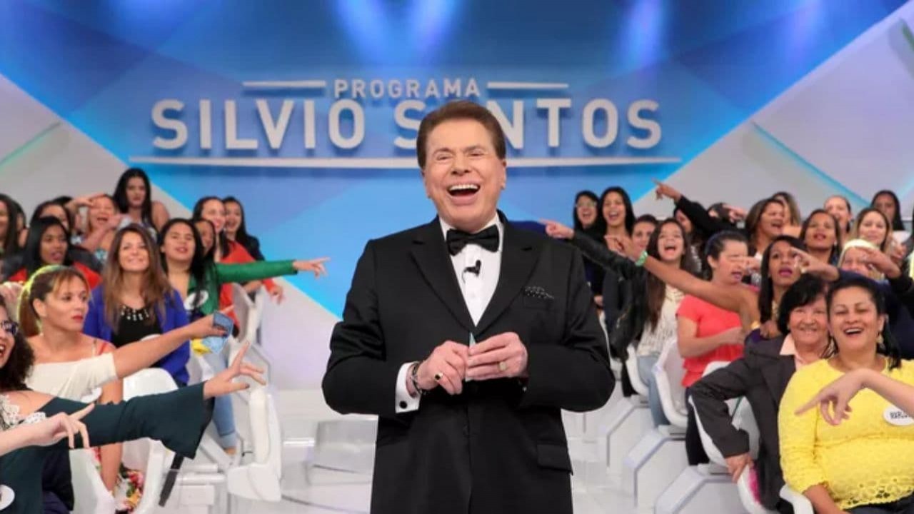 Silvio Santos de terno e gravata pretos, sorrindo, no palco do PSS