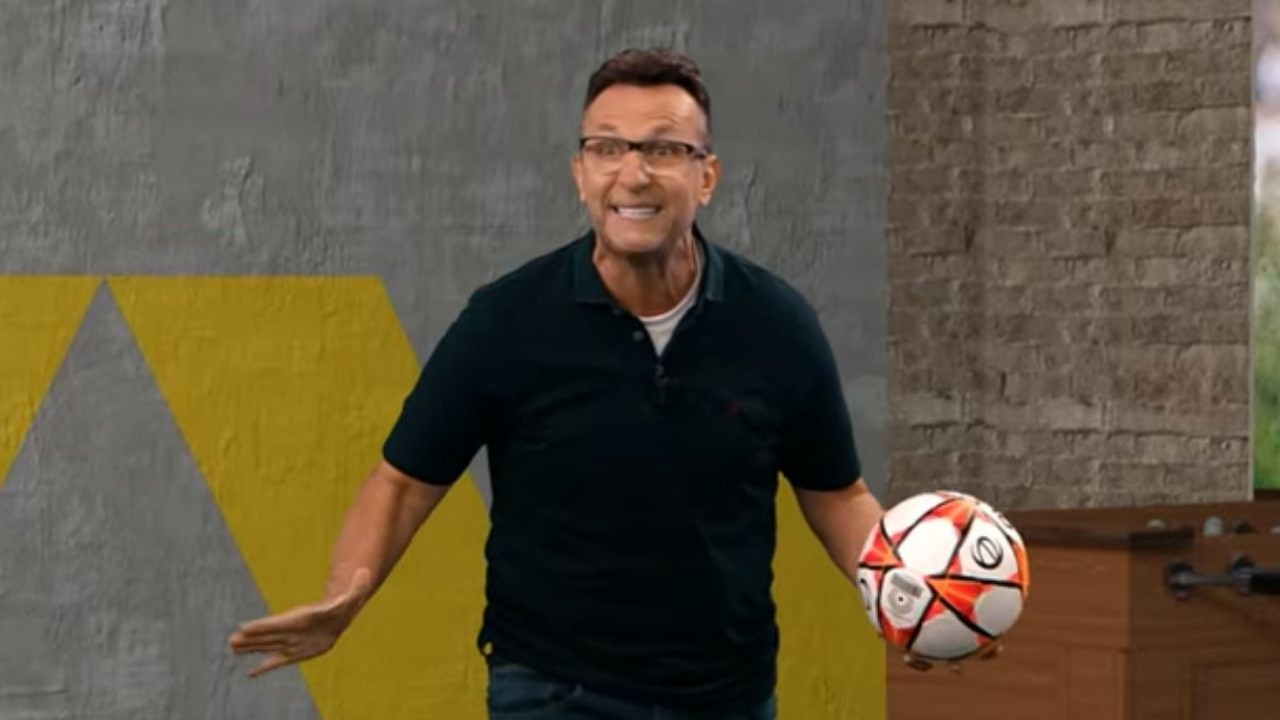 Neto de óculos e camiseta preta segurando bola de futebol com a mão esquerda