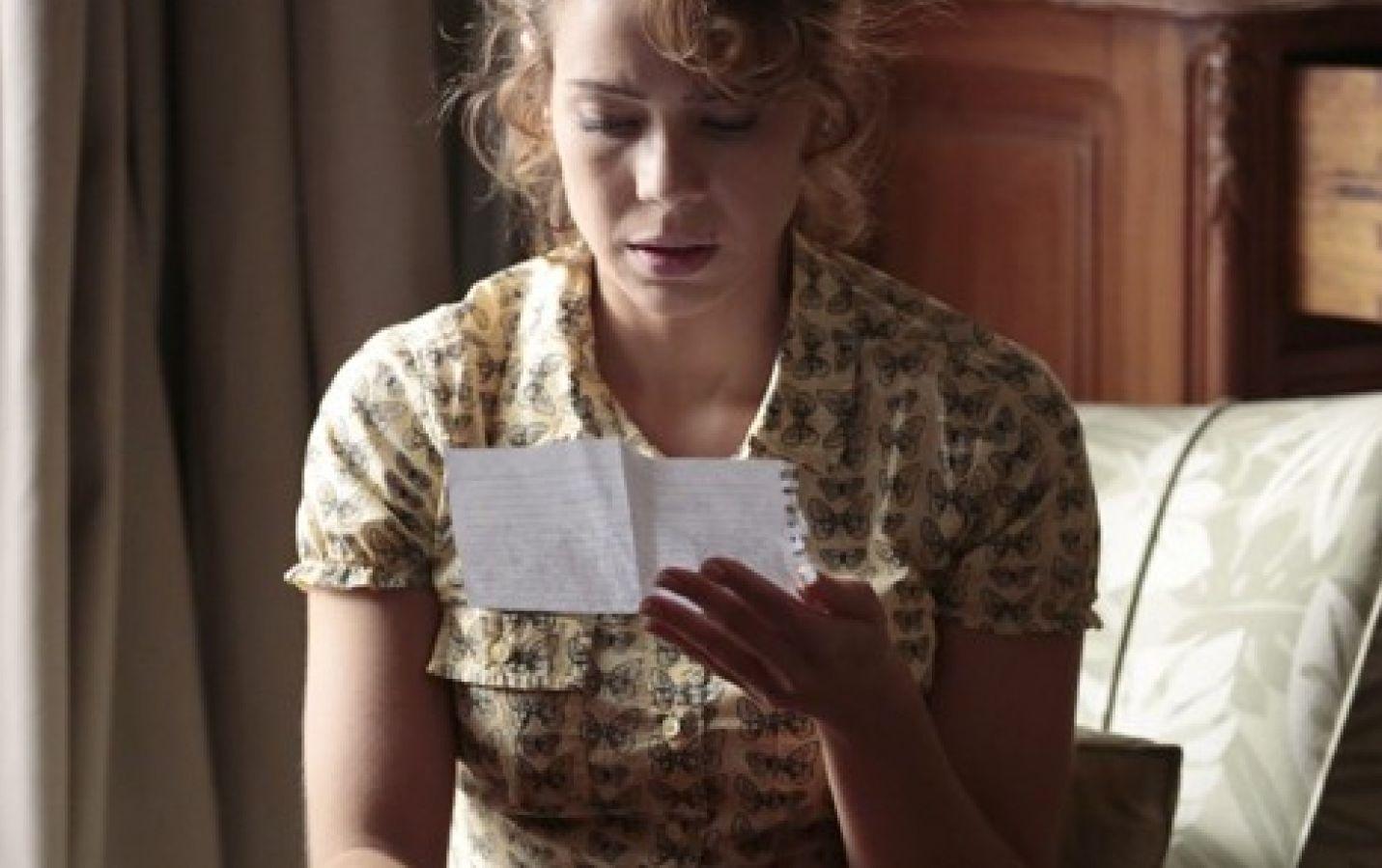 Cristina sentada na cama lendo carta 