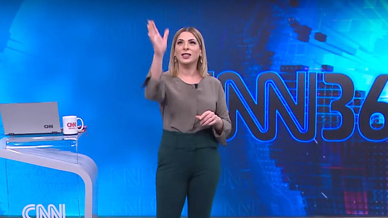 Daniela Lima com a mão levantada tentando pegar mosquito no estúdio da CNN 360