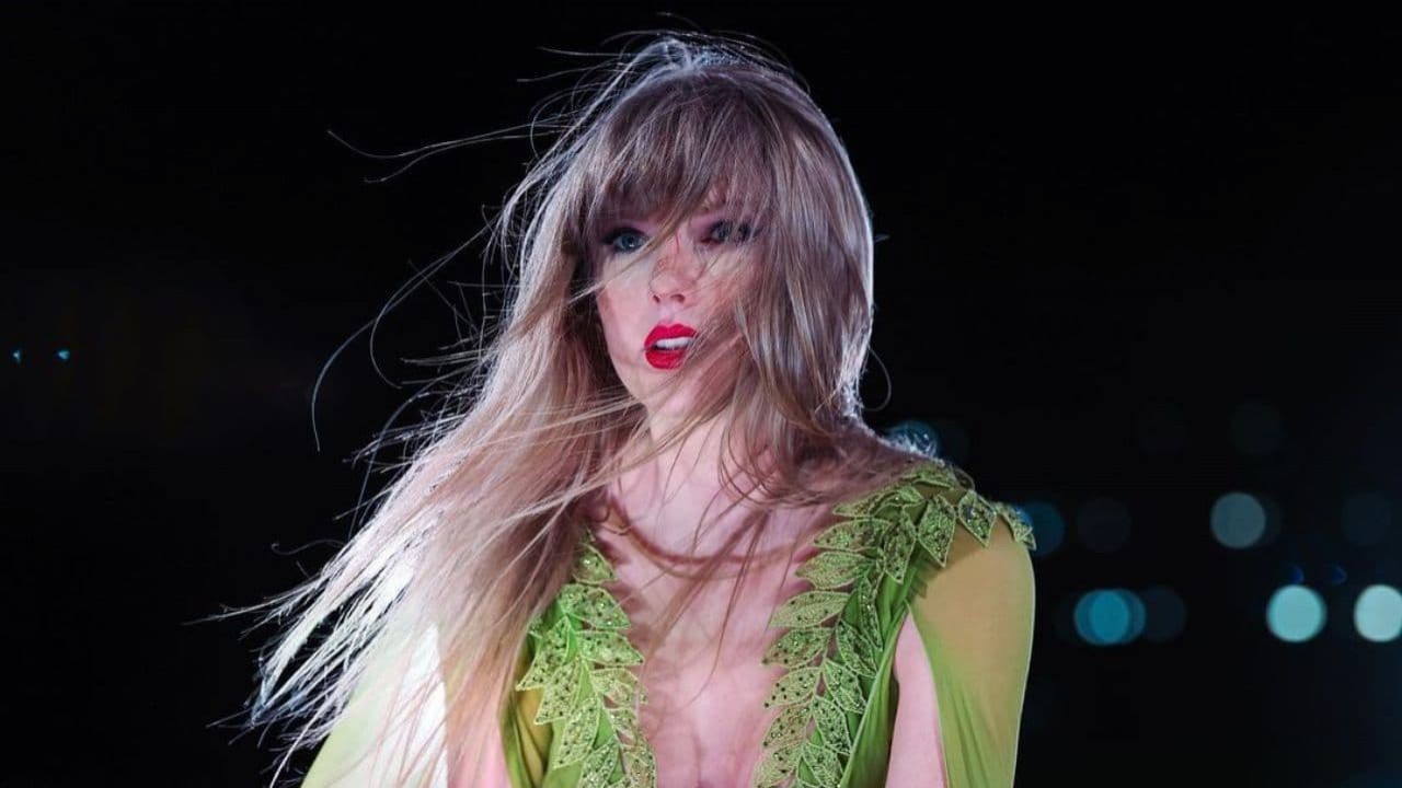 Taylor Swift com cabelos ao vento e roupa verde em show, fazendo carão