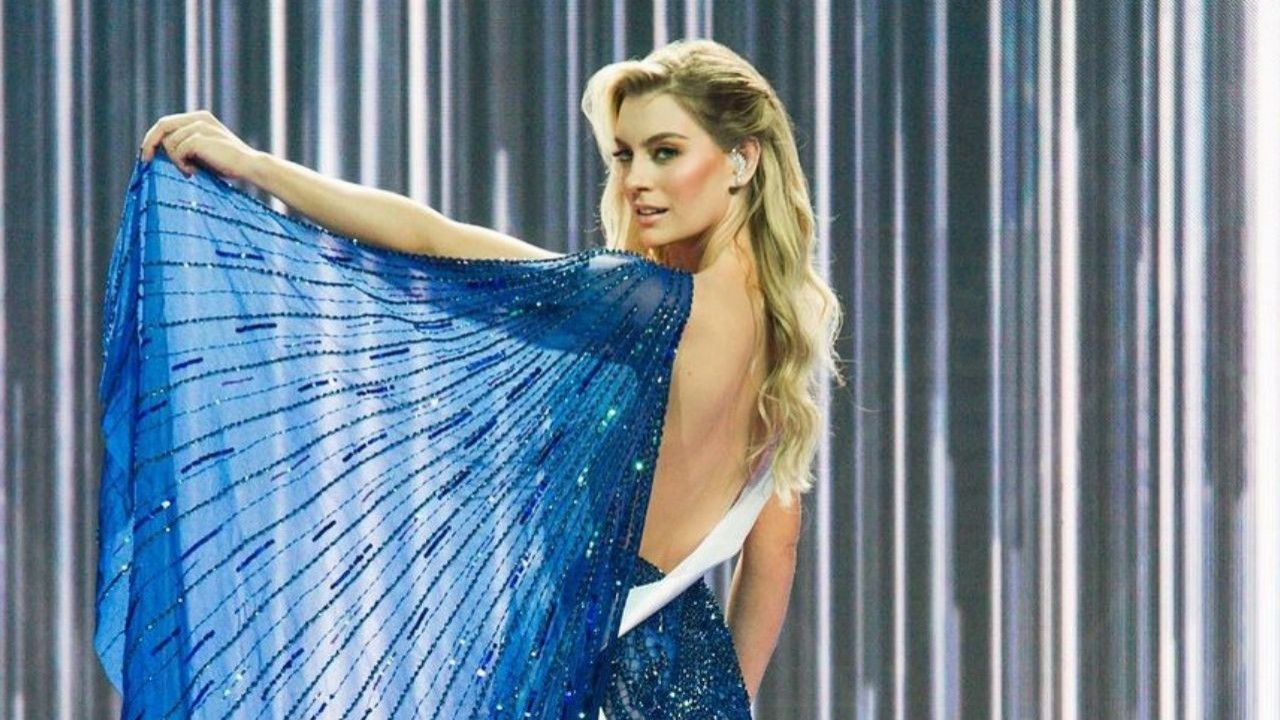 Miss Brasil 2021 de vestido azul posando para foto, cabelos loiros soltos