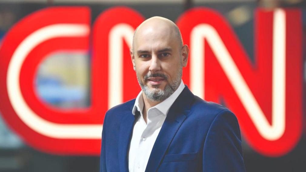 Douglas Tavolaro ao lado de uma TV com o logo CNN