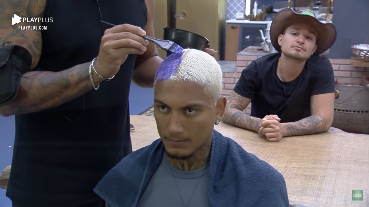Dynho Alves pintando o cabelo de roxo, sendo observado por MC Gui