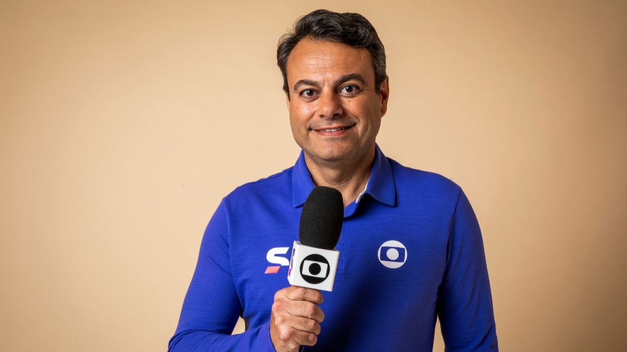 Eric Faria sorrindo, vestindo camisa azul do sportv e segurando microfone da Globo