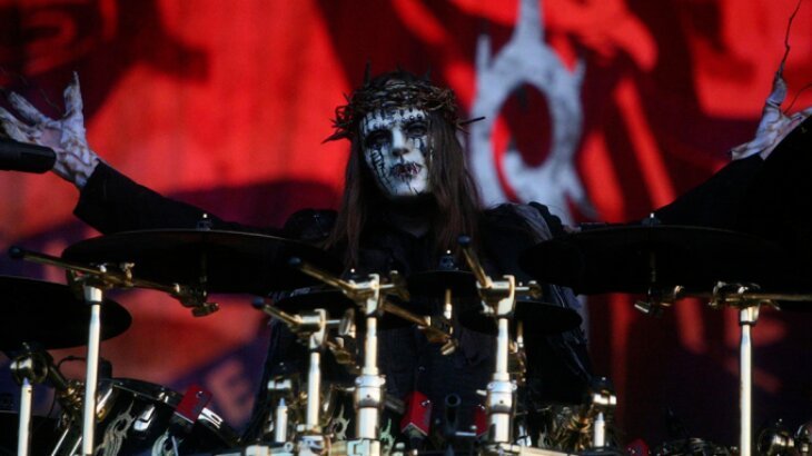 Joey Jordison de máscara e figurino, com os braços abertos, atrás da bateria