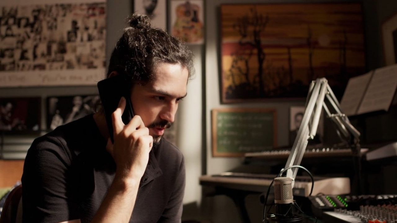 Gabriel Leone como Felipe em cena de Um Lugar ao Sol, de camisa preta, segurando telefone