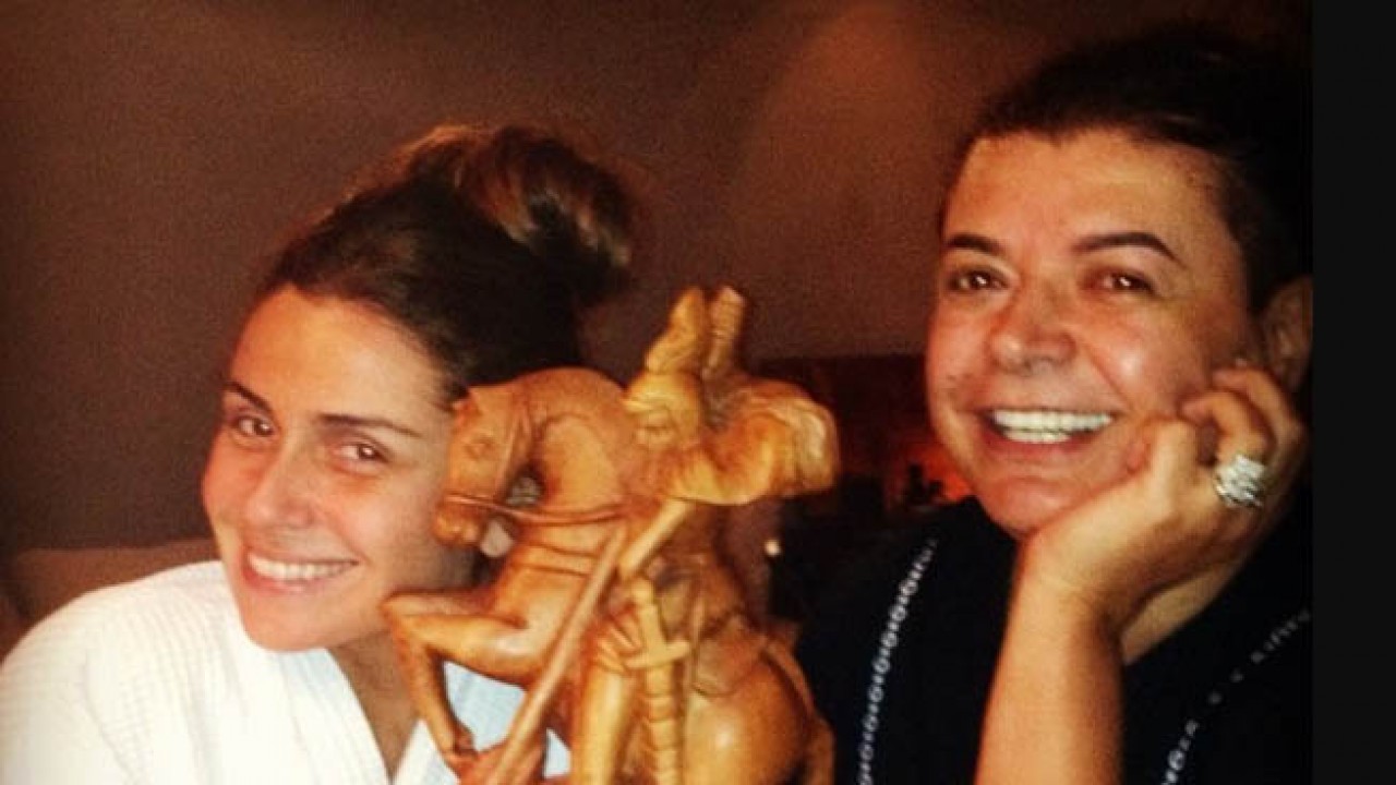 Giovanna Antonelli e David Brazil sorrindo juntos com estátua de São Jorge