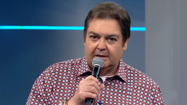 Faustão segurando microfone no palco do seu programa na Globo