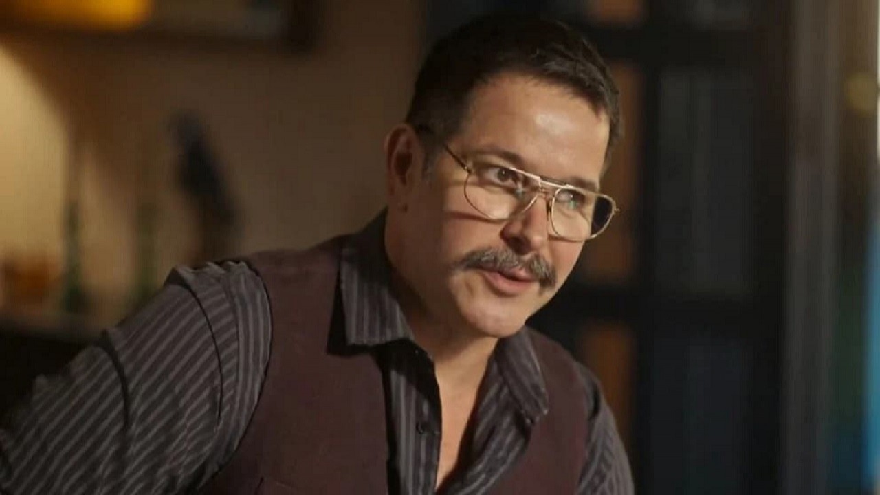 Murilo Benício como Tenório em Pantanal; personagem está sentado e usando óculos