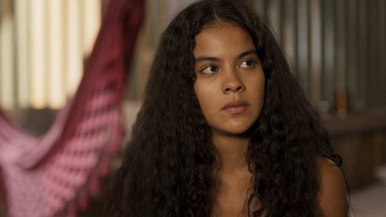 Bella Campos como Muda na novela Pantanal. Ela está sentada na fazenda