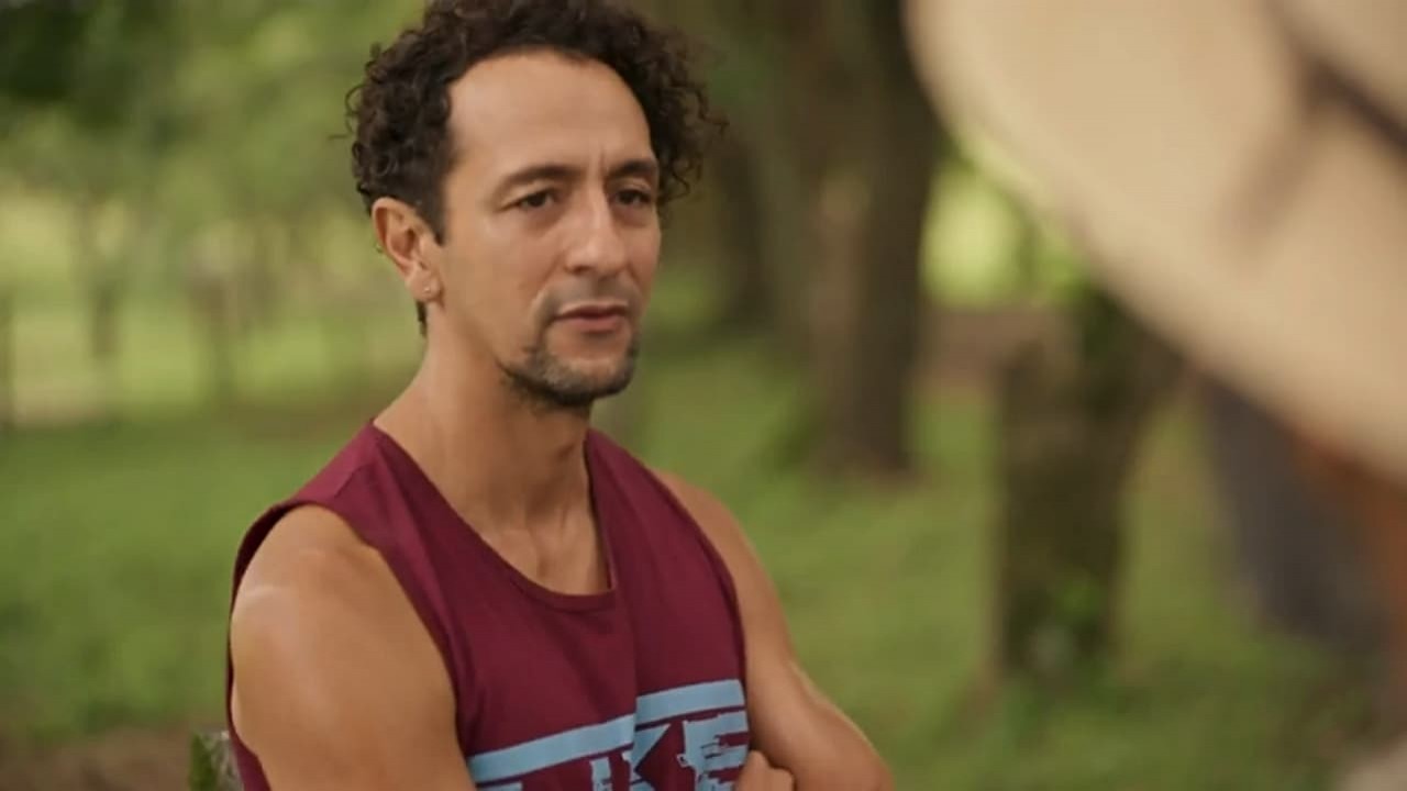 Irandhir Santos em cena na novela Pantanal como José Lucas. O personagem está em pé e de braços cruzados na fazenda