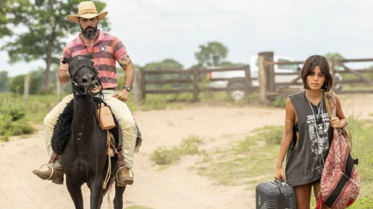 Juliano Cazarré como Alcides e Julia Dalavia como Guta em Pantanal. Ele está em cima de um cavalo e ela andando no meio da terra