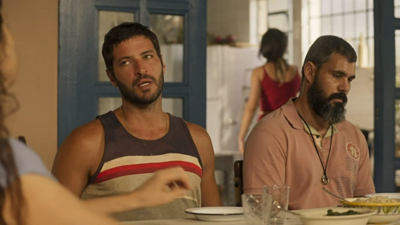 Leandro Lima e Juliano Cazarré como Levi e Alcides, respectivamente, na novela Pantanal. Os dois sentados na mesa