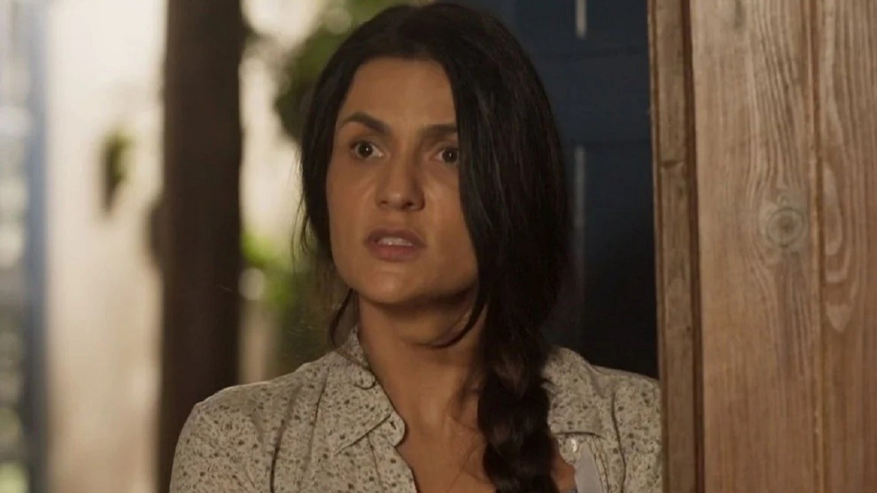 Paula Barbosa como Zefa em Pantanal; personagem está em pé escorada numa porta