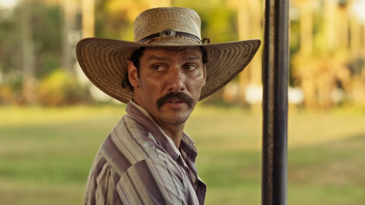 Guito como Tibério em cena da novela Pantanal, em exibição na Globo. Na imagem, o ator aparece usando um chapéu de peão em um cenário de fazenda ao fundo