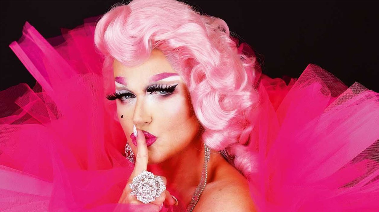 Xuxa vestida de drag queen colocando o dedo na boca 