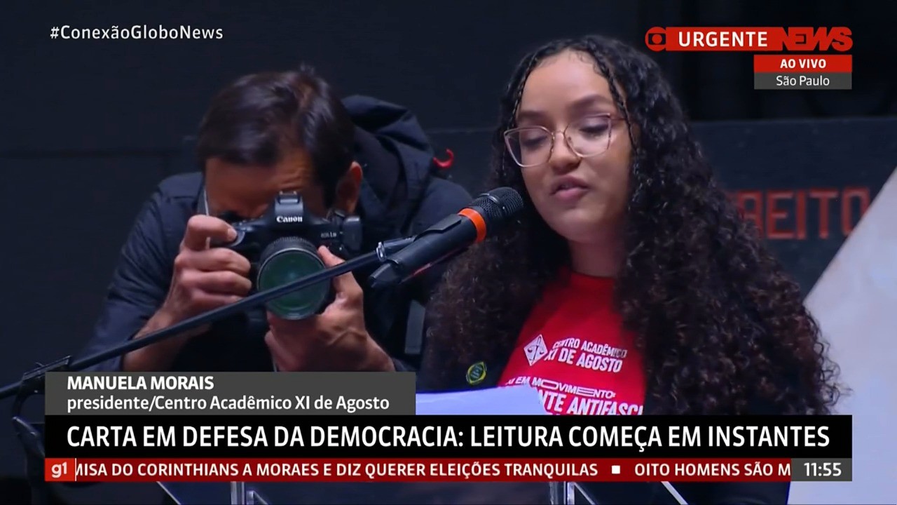 Mulher lendo carta em defesa da democracia com transmissão da GloboNews