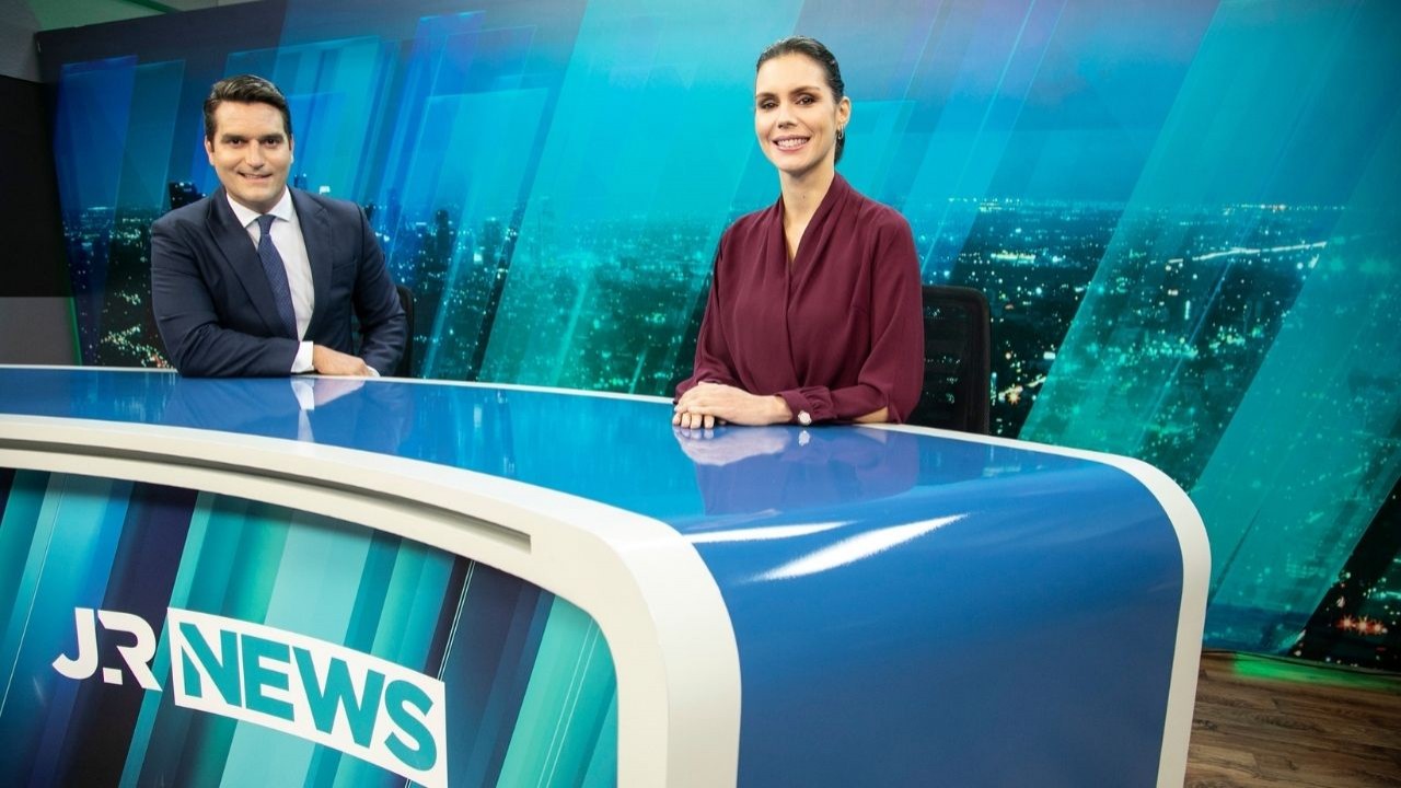 Gustavo Toledo e Camila Busnelli sorrindo na bancada do Jornal da Record News