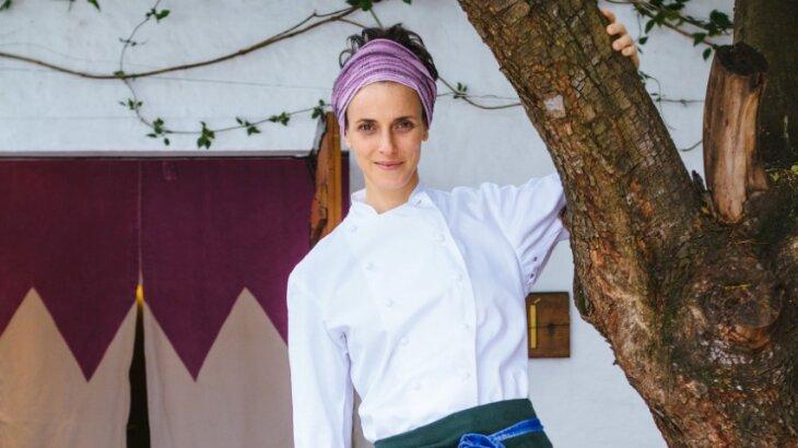 Com uniforme de chef, Helena Rizzo com a mão em uma árvore, posada para foto