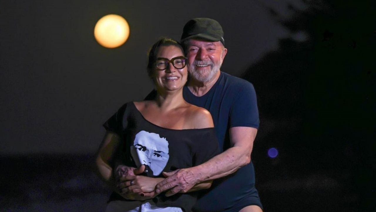 Janja e Lula abraçados e sorrindo em foto em que aparece a Lua na praia