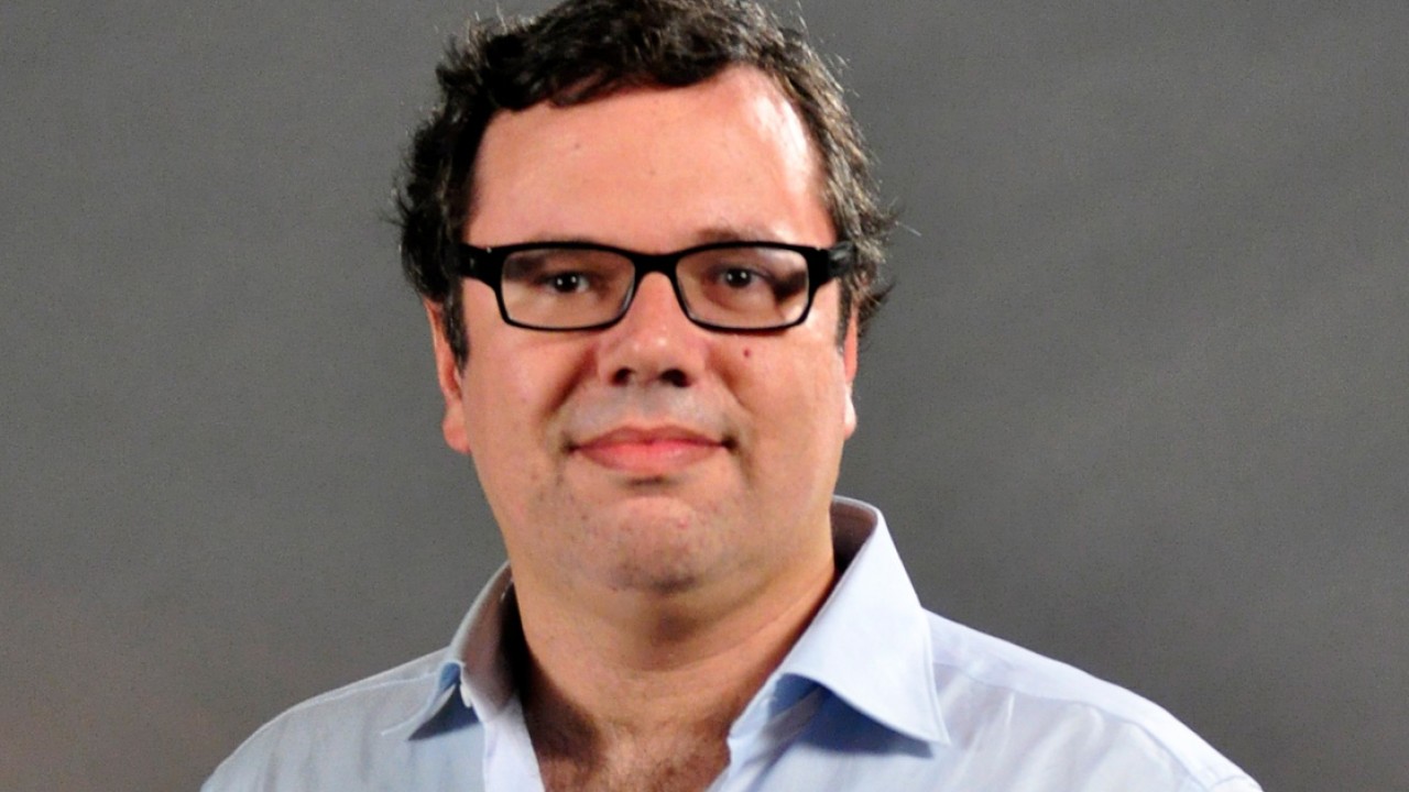 João Emanuel carneiro sorrindo timidamente de óculos
