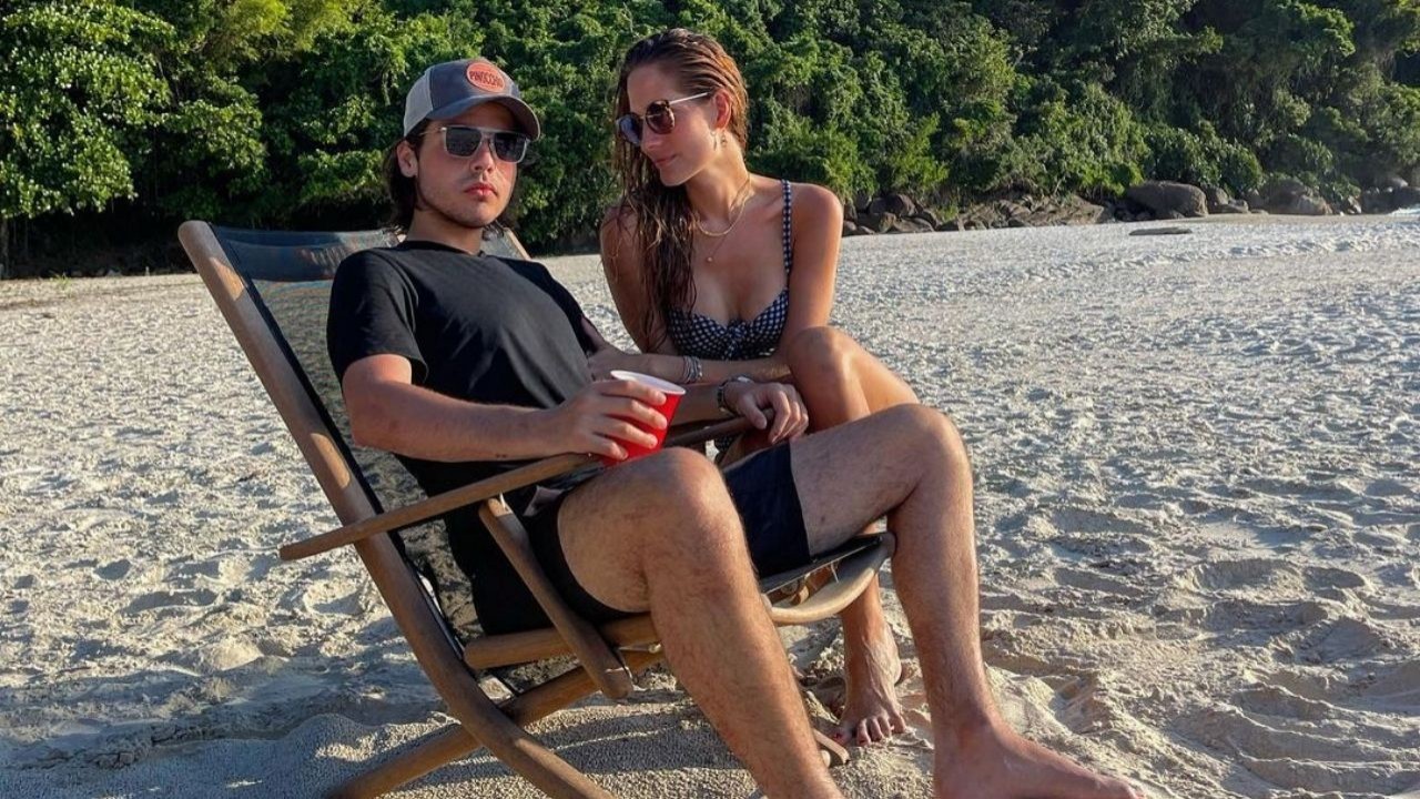 João Guilherme Silva sentado em cadeira de praia ao lado de namorada, Schynaider Moura