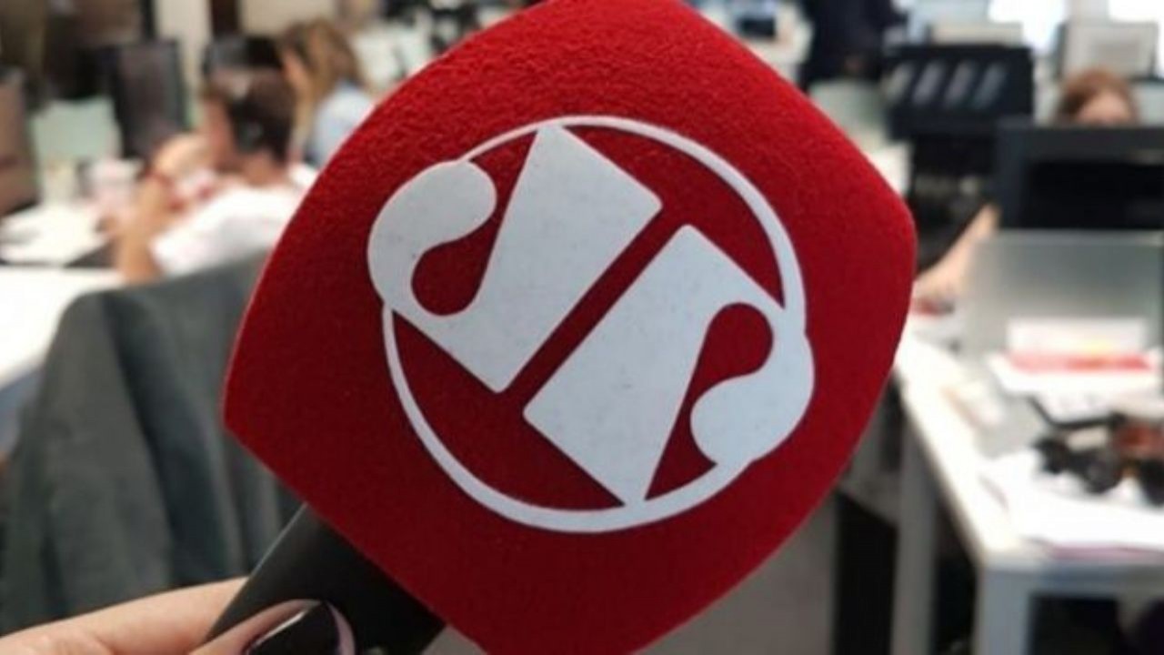 Microfone da Jovem Pan News em primeiro plano, com redação ao fundo