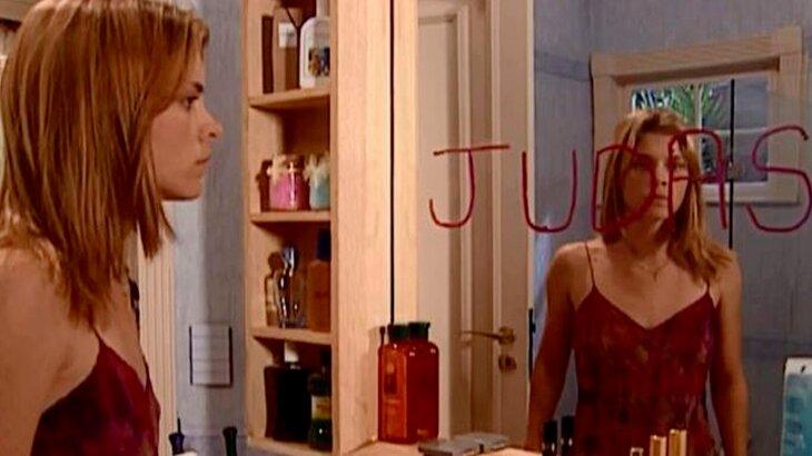 Camila olhando a palavra Judas no espelho do banheiro