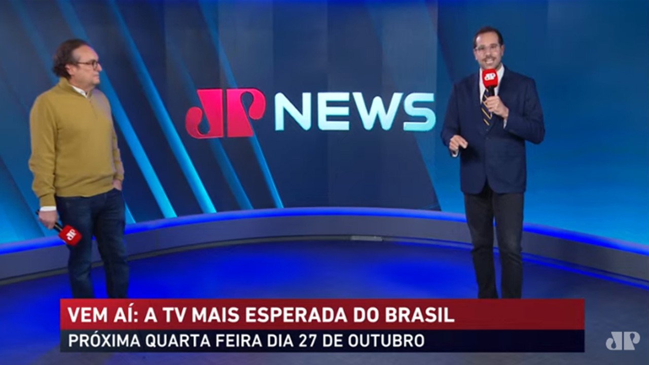 Tutinha Carvalho e Paulo Mathias no palco, diante do telão com o logo de Jovem Pan News