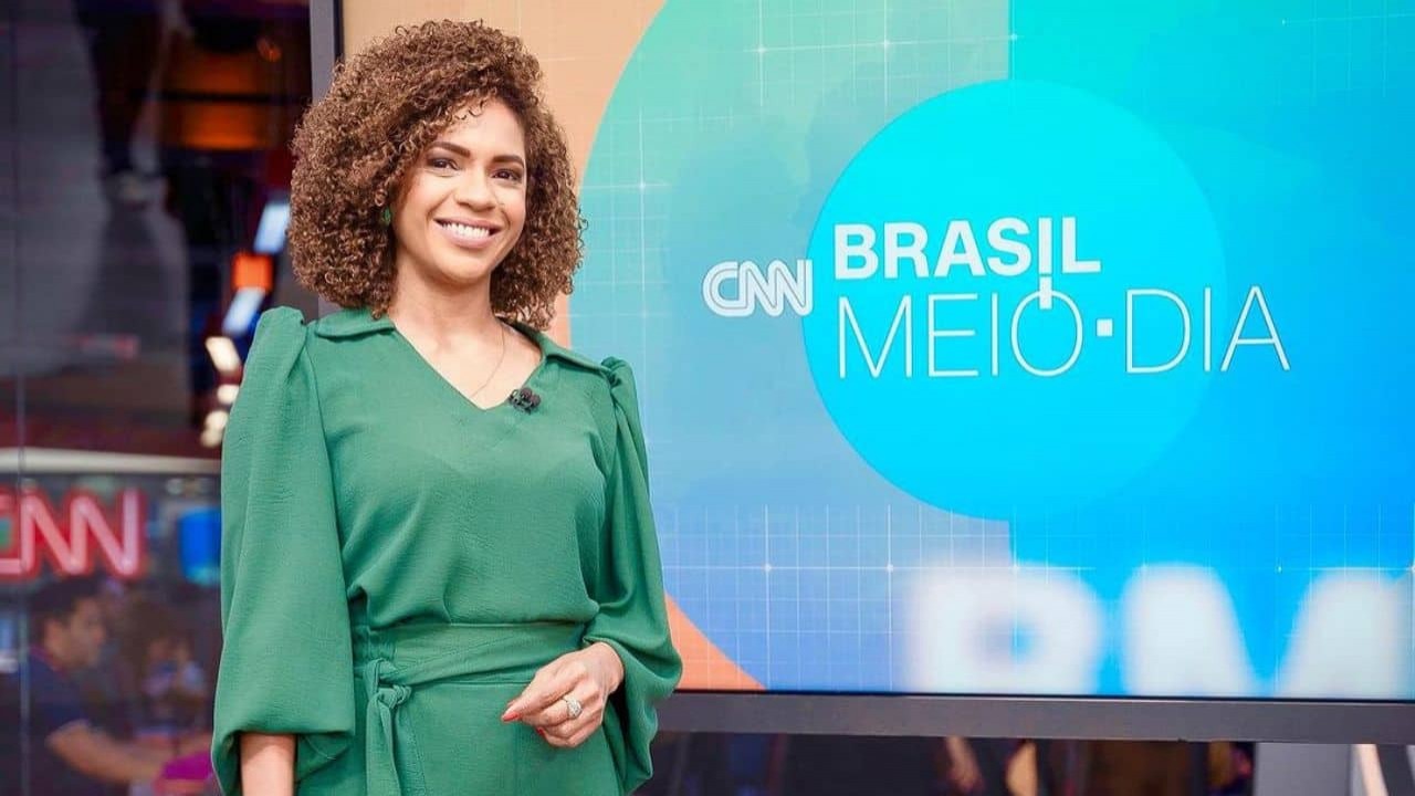 Luciana Barreto sorrindo, de roupa verde, posando no estúdio do Brasil Meio-Dia