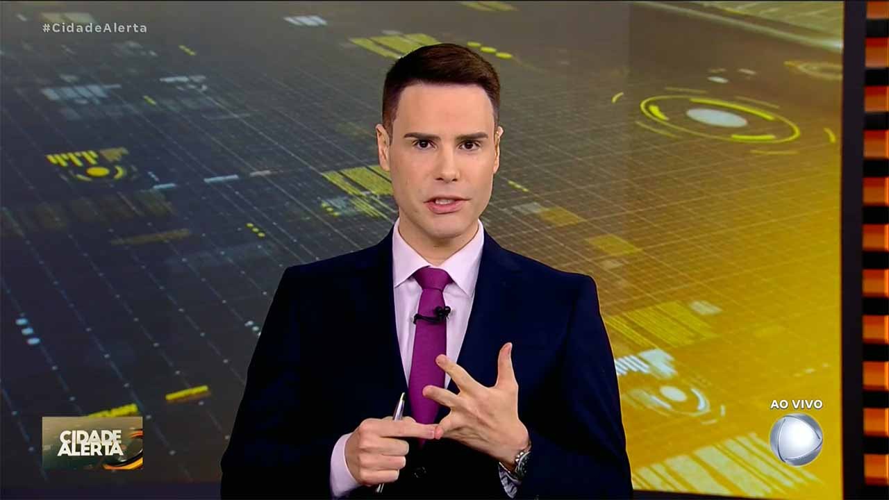 Luiz Bacci usando terno preto e gravata rosa no cenário do programa Cidade Alerta
