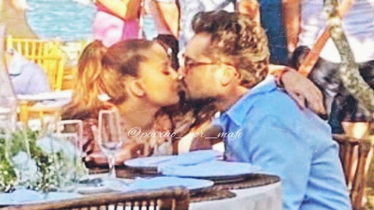 Maiara e Fernando Zor se beijam sentados em uma mesa do casamento do compositor Crystian Ribeiro