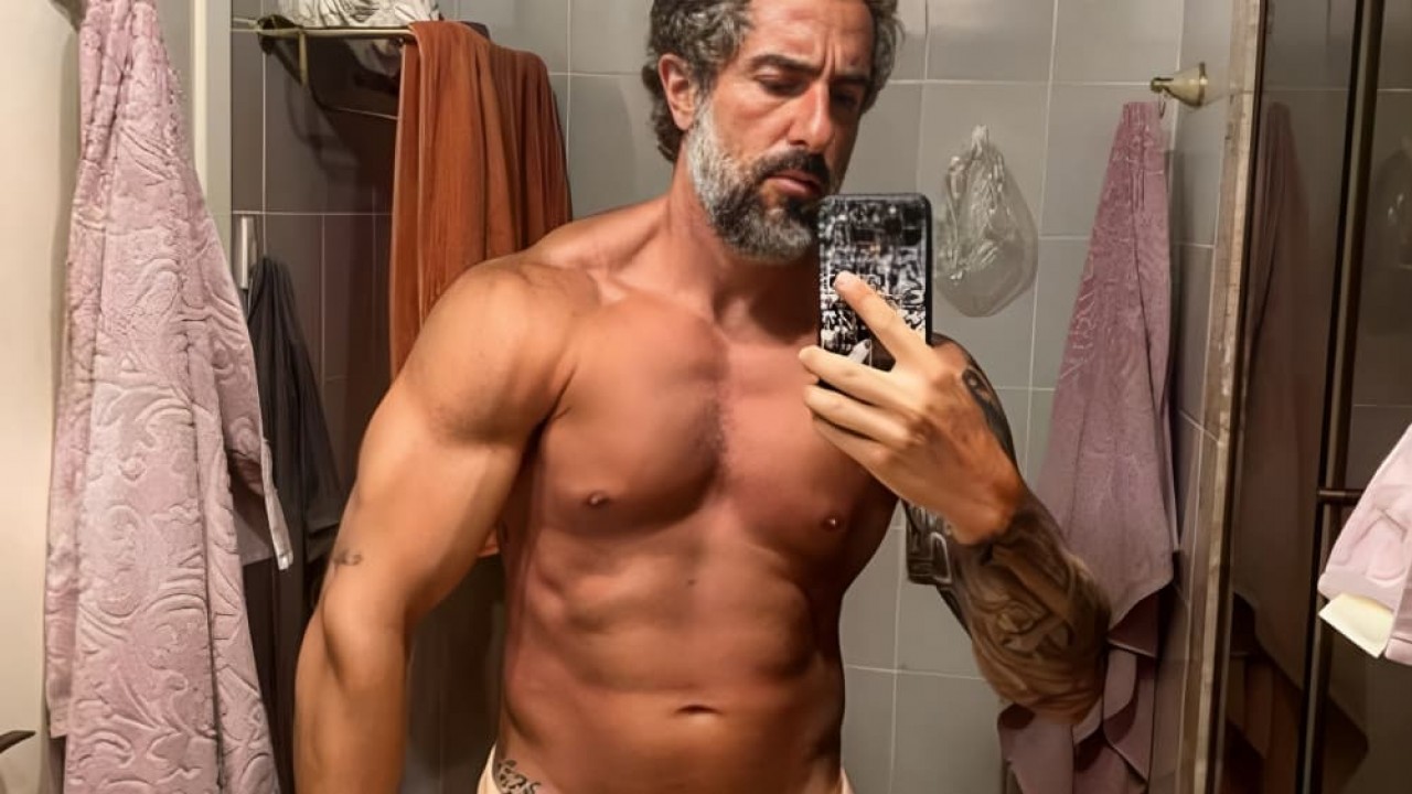 Marcos Mion posando sem camisa em foto no espelho, com expressão séria