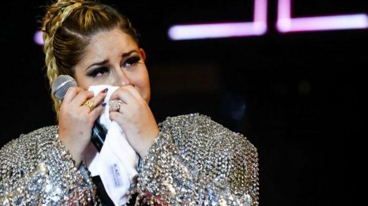 Marília Mendonça segurando microfone e limpando o rosto após chorar