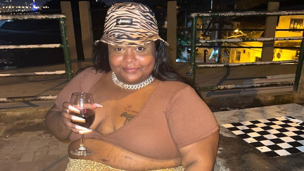MC Carol de Niterói com uma taça de vinho, um cordão prateado e a barriga de fora