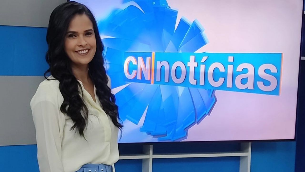 Elaine Cristina Santos de calça azul e camisa branca, no estúdio do CN Notícias, sorrindo