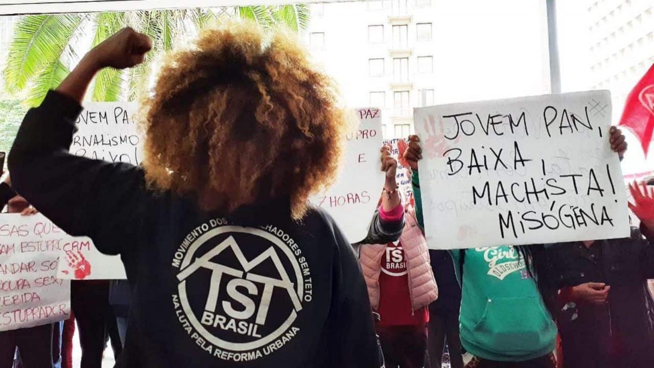 Mulher do MTST de costas para a foto e de frente para outras mulheres com cartazes de protesto