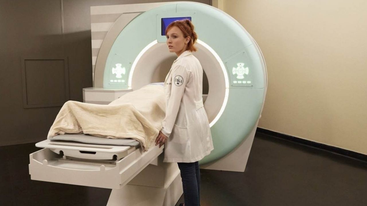 Larissa Manoela, caracterizada como médica, à beira de uma máquina de radiografia, com alguém deitado na máquina e coberto por um lençol