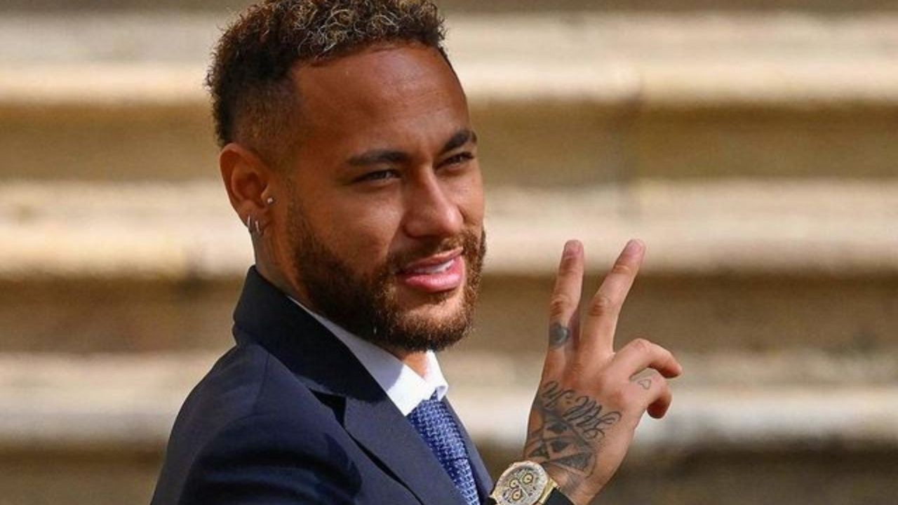 Neymar sorrindo e fazendo sinal de "paz e amor", de roupa social azul marinho